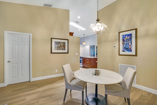 dining room with light hardwood / wood-style floors, high vaulted ceiling, and a chandelier