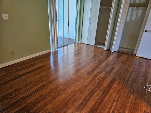 unfurnished bedroom with dark hardwood / wood-style flooring and multiple closets