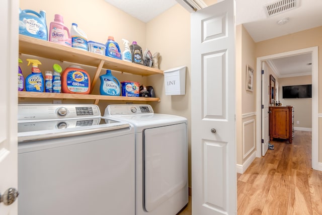 clothes washing area featuring light wood-type flooring, ornamental molding, and washing machine and dryer