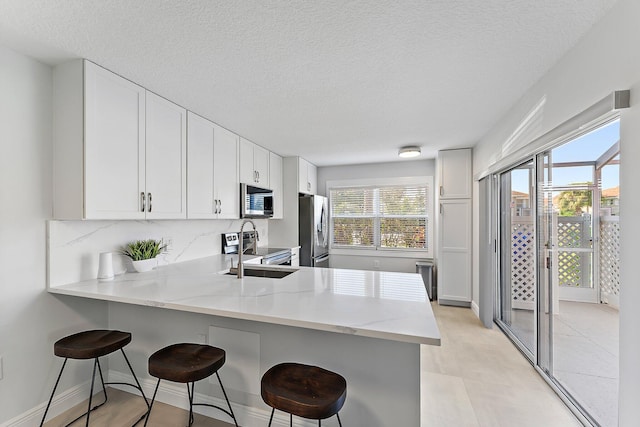 kitchen with a breakfast bar area, light stone counters, a peninsula, stainless steel appliances, and white cabinets