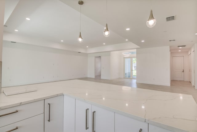 kitchen with decorative light fixtures, light stone counters, and white cabinetry