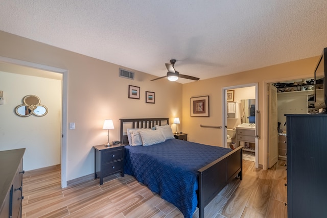 bedroom with light wood-type flooring, ensuite bath, ceiling fan, and a textured ceiling