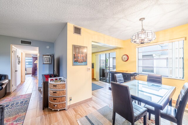 dining space with a textured ceiling, a notable chandelier, and light hardwood / wood-style flooring