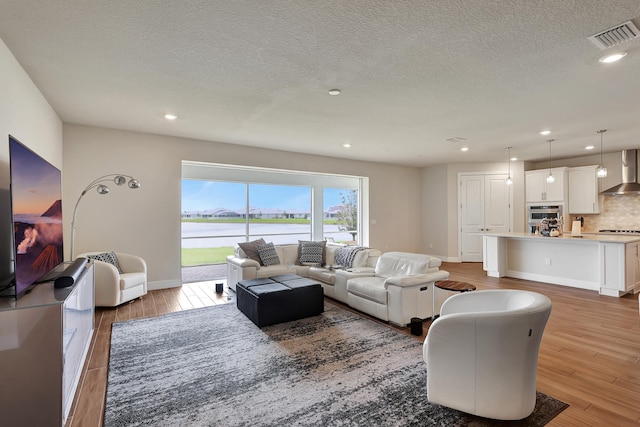 living room with a water view, light hardwood / wood-style floors, and a textured ceiling