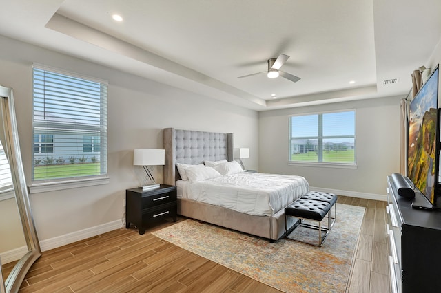 bedroom featuring light wood-type flooring, ceiling fan, and a raised ceiling