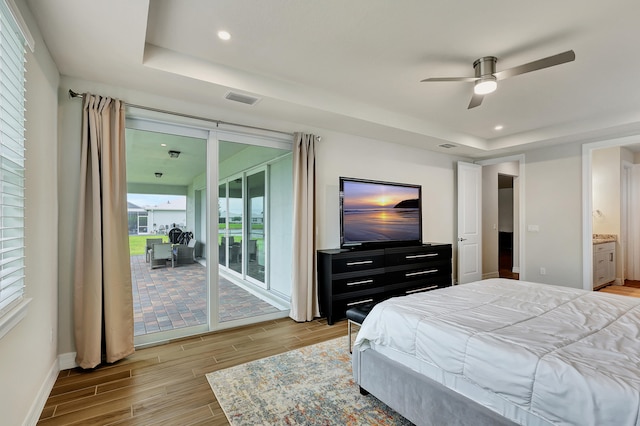 bedroom with ensuite bathroom, ceiling fan, a tray ceiling, light hardwood / wood-style flooring, and access to outside