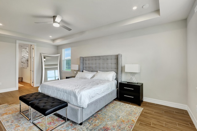 bedroom with a raised ceiling, light wood-type flooring, and ceiling fan