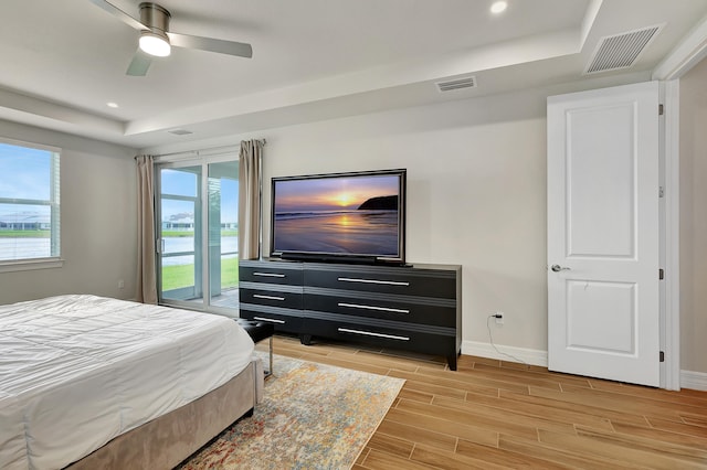 bedroom featuring light wood-type flooring, ceiling fan, a tray ceiling, and access to outside