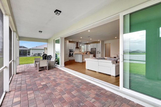 view of patio featuring glass enclosure and a water view