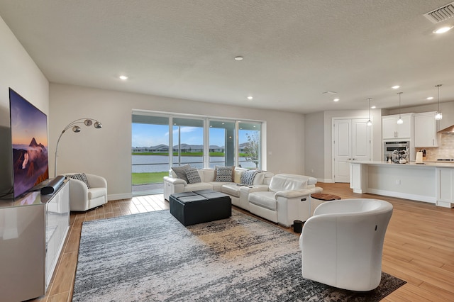 living room with a water view, light wood-type flooring, and a textured ceiling