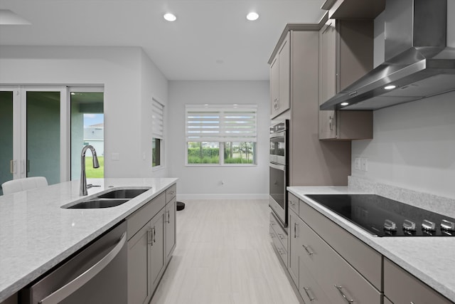 kitchen with light stone counters, gray cabinetry, wall chimney exhaust hood, sink, and appliances with stainless steel finishes