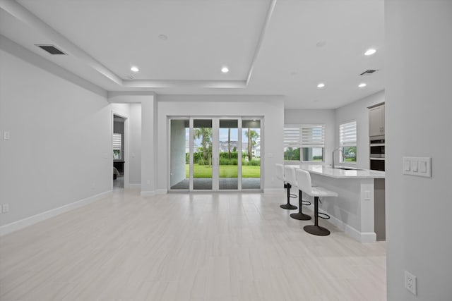 interior space featuring stainless steel double oven, a center island with sink, a breakfast bar area, and a tray ceiling