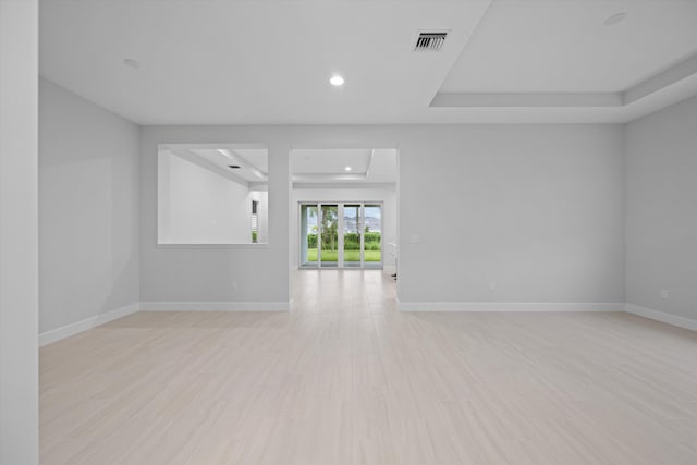 spare room with a raised ceiling and light hardwood / wood-style flooring