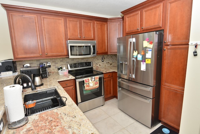 kitchen with light stone counters, light tile patterned floors, appliances with stainless steel finishes, and tasteful backsplash