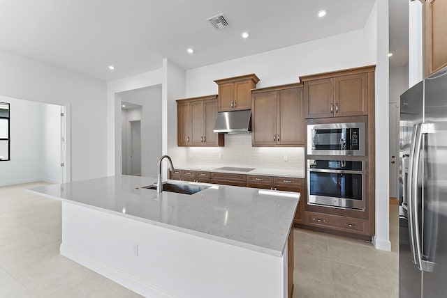 kitchen featuring appliances with stainless steel finishes, sink, backsplash, a kitchen island with sink, and light stone countertops