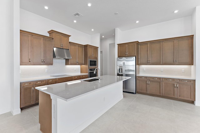 kitchen featuring sink, a kitchen island with sink, stainless steel appliances, light stone counters, and tasteful backsplash