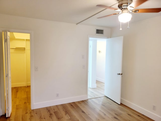 unfurnished bedroom with a spacious closet, light hardwood / wood-style floors, a closet, and ceiling fan