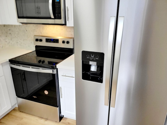 kitchen featuring light wood-type flooring, decorative backsplash, white cabinetry, and stainless steel appliances