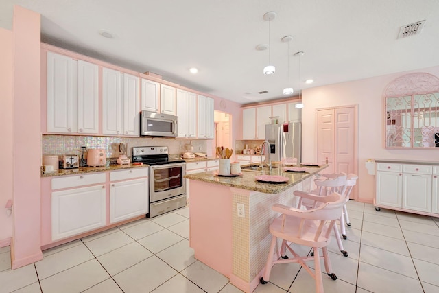 kitchen featuring white cabinets, hanging light fixtures, sink, a center island with sink, and stainless steel appliances