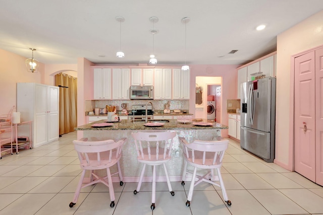 kitchen with an island with sink, stainless steel appliances, tasteful backsplash, decorative light fixtures, and washer / clothes dryer