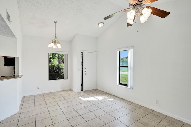 empty room featuring light tile patterned flooring, ceiling fan with notable chandelier, high vaulted ceiling, and a textured ceiling