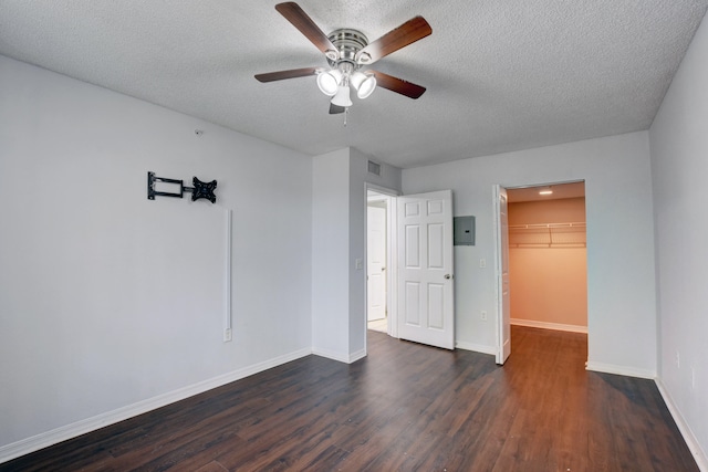 unfurnished bedroom featuring ceiling fan, a spacious closet, a closet, dark hardwood / wood-style floors, and a textured ceiling