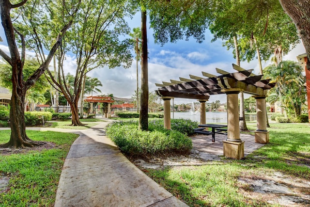 view of community featuring a water view, a lawn, and a pergola