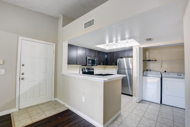 kitchen with light tile patterned flooring, dark brown cabinetry, stainless steel appliances, kitchen peninsula, and washing machine and dryer