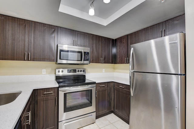 kitchen with light stone counters, dark brown cabinetry, a raised ceiling, light tile patterned flooring, and appliances with stainless steel finishes