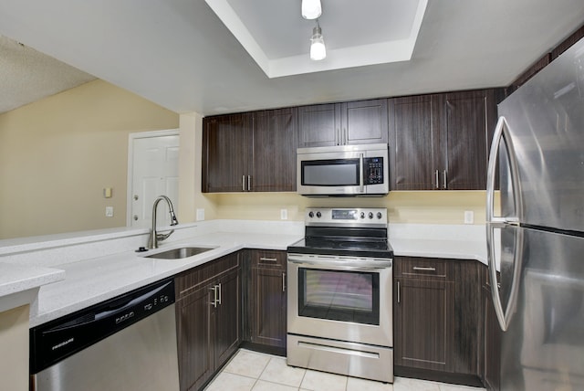 kitchen with dark brown cabinets, a raised ceiling, sink, stainless steel appliances, and light tile patterned floors