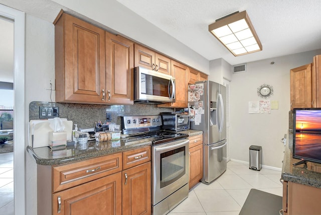 kitchen with light tile patterned flooring, backsplash, appliances with stainless steel finishes, and dark stone countertops