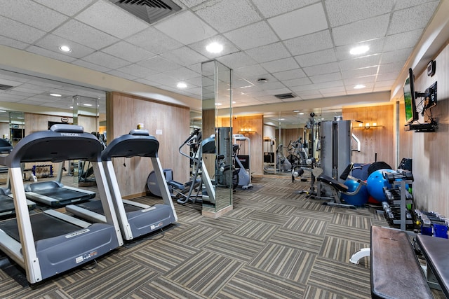 exercise room featuring a paneled ceiling, wooden walls, and dark carpet