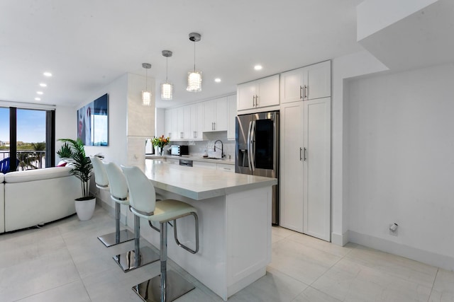 kitchen featuring a kitchen breakfast bar, stainless steel refrigerator with ice dispenser, pendant lighting, decorative backsplash, and white cabinets