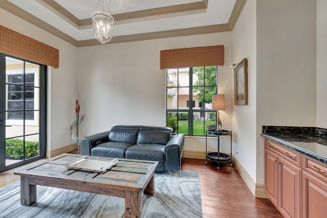 living room with dark wood-type flooring, a raised ceiling, a notable chandelier, and crown molding