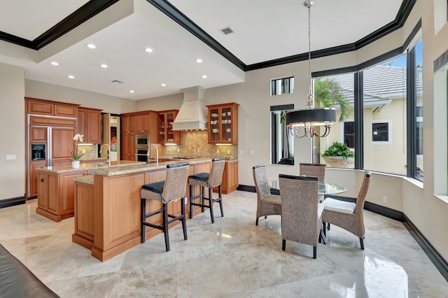 kitchen featuring light stone counters, a chandelier, custom range hood, a large island with sink, and a kitchen breakfast bar