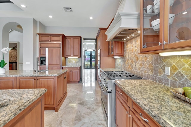 kitchen with high end appliances, light stone countertops, custom range hood, sink, and tasteful backsplash