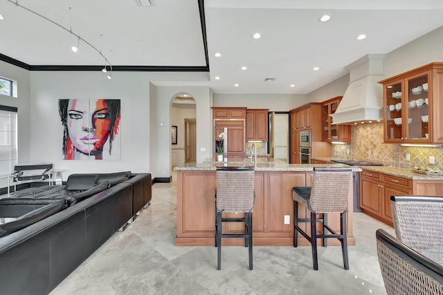 kitchen with a kitchen breakfast bar, a large island with sink, built in appliances, and light stone counters