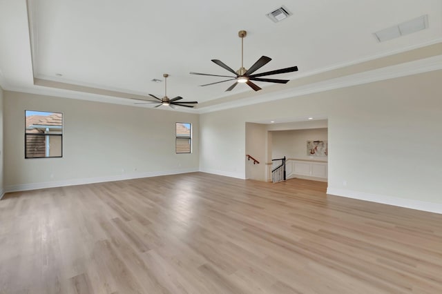 empty room with ornamental molding, light hardwood / wood-style flooring, and a tray ceiling