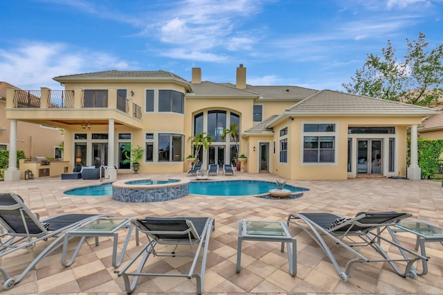 rear view of house with a pool with hot tub, a balcony, a patio, and french doors