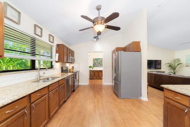 kitchen with appliances with stainless steel finishes, sink, vaulted ceiling, light stone counters, and light hardwood / wood-style flooring