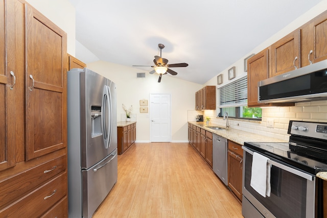 kitchen with sink, stainless steel appliances, lofted ceiling, light stone counters, and light hardwood / wood-style flooring