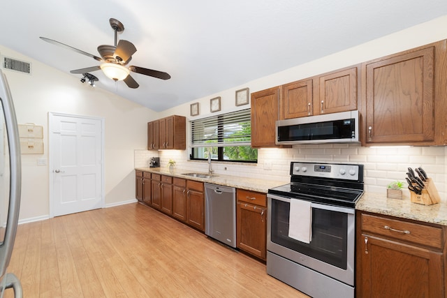 kitchen with lofted ceiling, backsplash, light wood-type flooring, sink, and stainless steel appliances