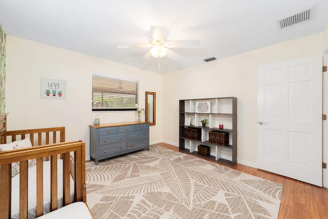 bedroom featuring ceiling fan, light hardwood / wood-style floors, and a nursery area