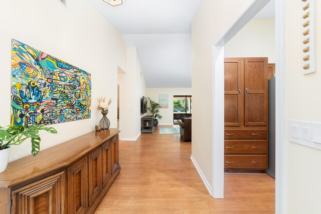 hall with baseboards, light wood finished floors, and vaulted ceiling