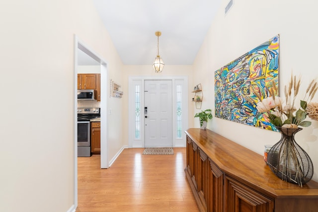 entryway with baseboards, lofted ceiling, light wood-style flooring, and visible vents