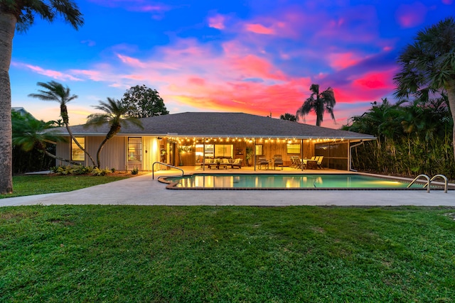 pool at dusk with a patio and a lawn