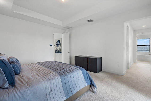 bedroom featuring light colored carpet, a tray ceiling, and ensuite bath