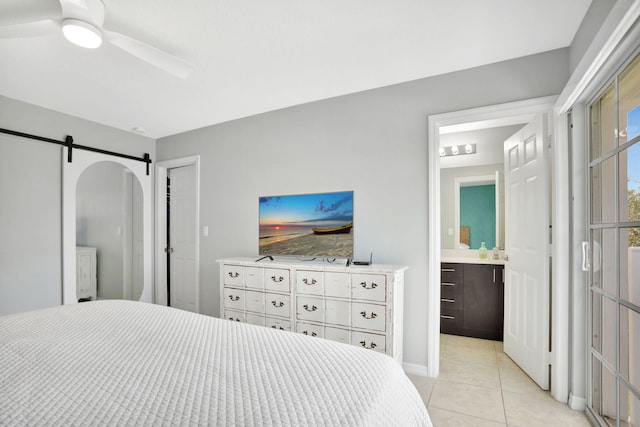 bedroom featuring a barn door, ensuite bathroom, ceiling fan, and light tile patterned floors