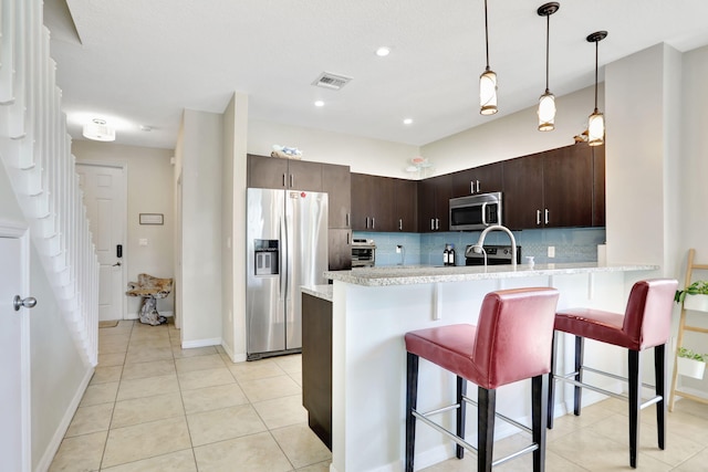 kitchen featuring decorative backsplash, appliances with stainless steel finishes, dark brown cabinets, a kitchen bar, and kitchen peninsula