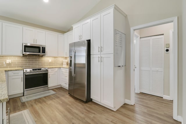 kitchen featuring white cabinets, light stone counters, vaulted ceiling, light hardwood / wood-style flooring, and stainless steel appliances